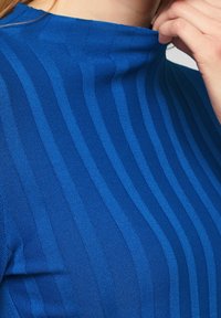Blå ribbad stickad topp med hög halsringning, med växelvis breda och smala texturerade ränder, med en kroppsnära passform.