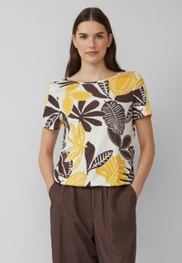 Haut à manches courtes, col rond, avec un motif floral jaune et marron sur fond blanc, fabriqué en tissu léger.