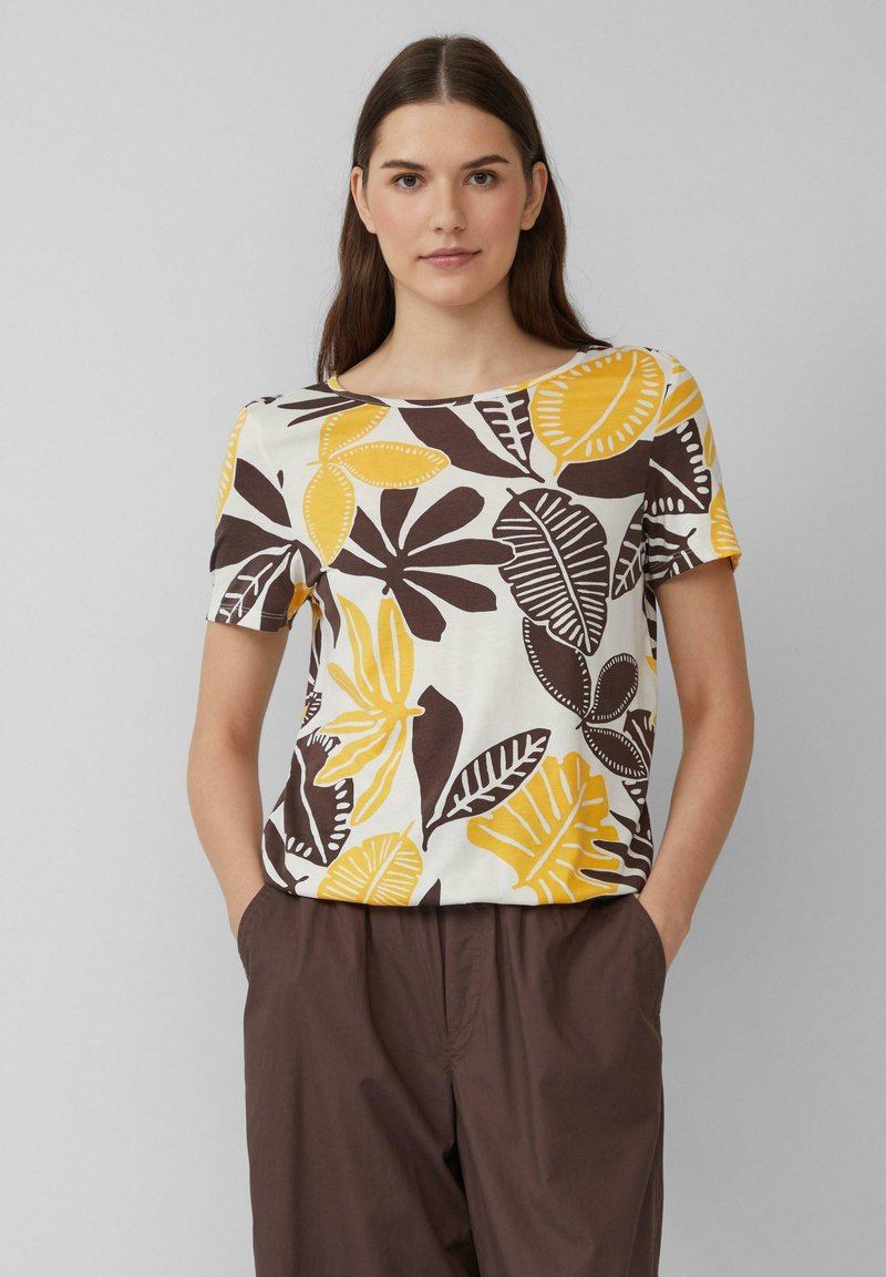 Haut à manches courtes, col rond, avec un motif floral jaune et marron sur fond blanc, fabriqué en tissu léger.
