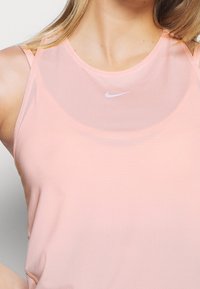Roze Nike sporttop met ronde hals, mesh textuur en klein wit logo op de borst. Verstelbare banden.
