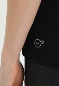 Svart sporttop med en mjuk textur. Har en "DRY CELL"-logotyp i vitt nära fållen. Närbild av armen och sömmen på sidan synlig.