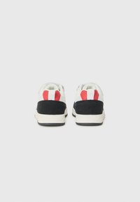 Hvite sneakers med svarte semskede hælakkenter og rød-hvit stripete detalj på hælen. Har gummisåle og polstret krage.