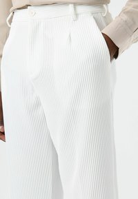 Witte broek met krijtstreep, gemaakt van lichtgewicht stof, voorzien van een tailleband met riemlussen, steekzakken aan de voorkant en een licht geplooid ontwerp.