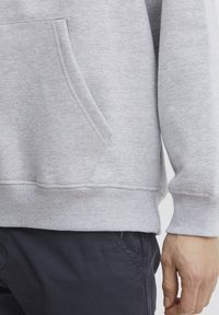 Gray sweatshirt with a front pocket, ribbed hem and cuffs, made of soft fabric. Paired with dark pants, showcasing a casual style.