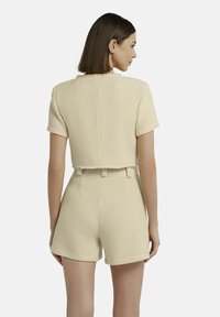 Beige strukturiertes Zweiteiler-Outfit mit einem kurzärmeligen, cropped Oberteil und hochgeschnittenen Shorts, das durch einen sauberen Schnitt und minimale Details besticht.