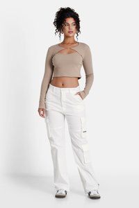 Beigerippiger, langärmliger Cropped-Top mit Ausschnitt-Detail, kombiniert mit weißen Cargo-Hosen, die mehrere Taschen und einen lockeren Schnitt haben.