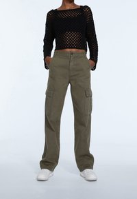 Haut noir en maille courte à manches longues avec un pantalon cargo vert olive doté de grandes poches latérales, porté avec des baskets blanches.