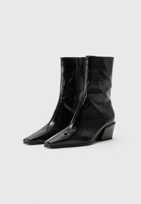 Bottines noires en matériau brillant et texturé avec un bout pointu et un petit talon carré, dotées d'une fermeture éclair sur le devant.
