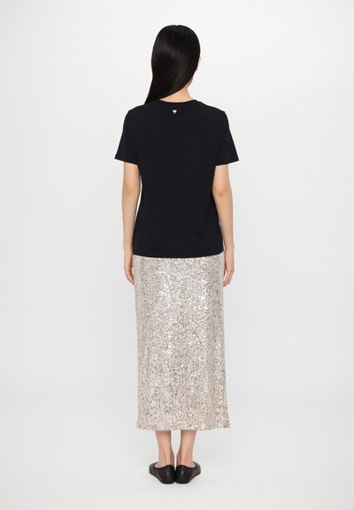 Sort T-shirt med korte ærmer og rund hals, kombineret med en længde lang, skinnende paillet nederdel i lys guld. Sorte slip-on sko.