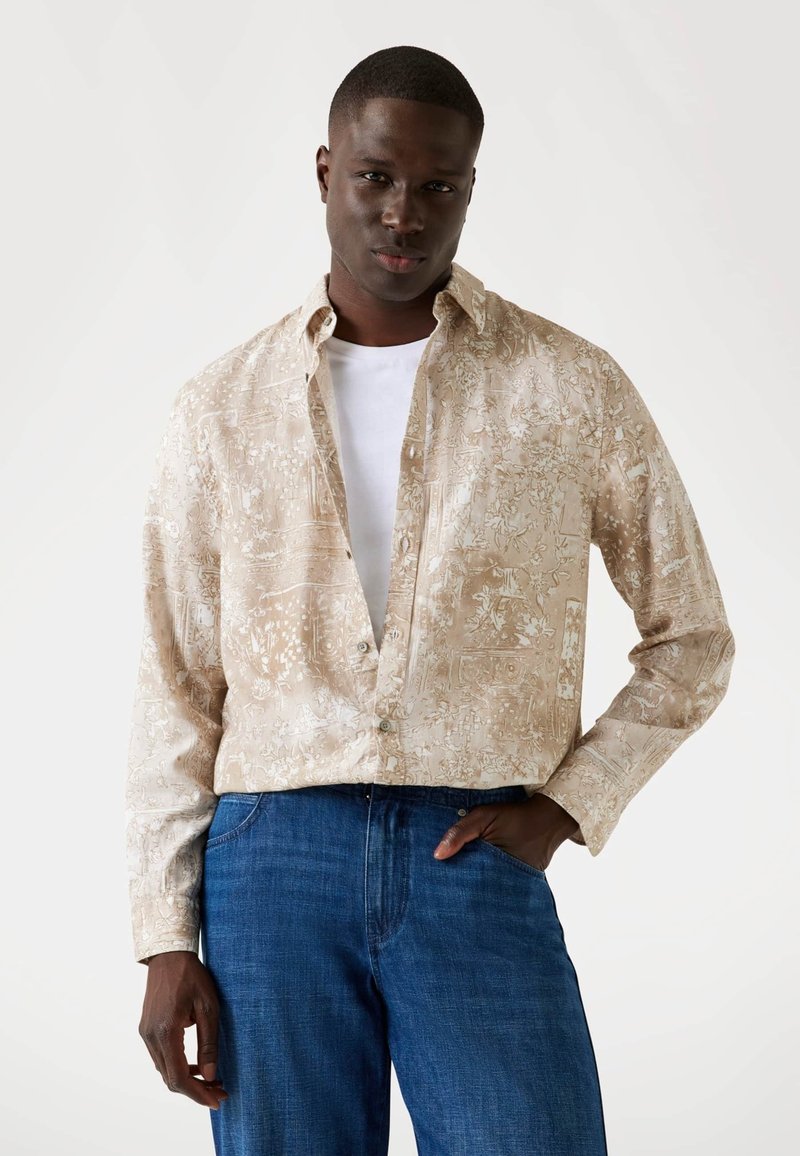 Korte mouwen overhemd van beige stof met witte bloemmotieven, comfortabele pasvorm en button-down kraag, gecombineerd met blauwe denim jeans.
