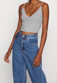 Haut court gris côtelé à fines bretelles, associé à un jean en denim bleu taille haute avec braguette à boutons et design classique à 5 poches.