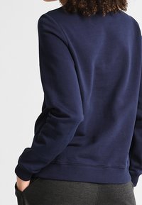 Felpa blu navy realizzata in morbido tessuto, con colletto a girocollo, maniche lunghe, polsini a costine e una vestibilità comoda con una texture liscia.