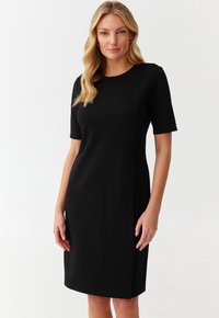 Crna haljina kratkih rukava s okruglim izrezom, ravnog kroja i bočnim prorezima. Izrađena od glatkog materijala, pruža elegantno pristajanje cijelim tijelom.