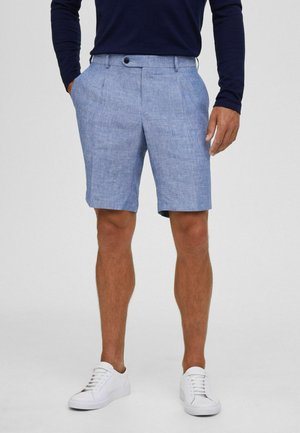 Pantalones cortos texturizados en azul claro, con un diseño de parte delantera plana, bolsillos laterales y un cierre de botón único, combinados con zapatillas blancas.