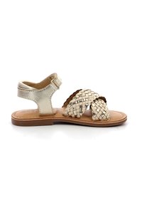 Sandalias de oro claro con tiras trenzadas, hebilla en el tobillo y suela marrón. Textura de cuero suave, diseño abierto y tacón plano para mayor comodidad.