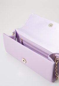 Λιλά δερμάτινη τσάντα χειρός με χρυσό κούμπωμα, εσωτερική τσέπη και αλυσίδα. Μαλακή υφή, μινιμαλιστικός σχεδιασμός, άποψη από την ανοιχτή κορυφή.