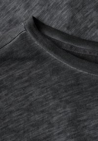 T-shirt gris foncé en tissu avec une texture légèrement chinée, présentant un col rond et un matériau lisse et flexible.