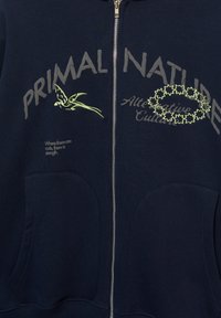 Navy zip-up hoodie featuring gray and light green text, two front pockets, and soft textured fabric with embroidered accents.