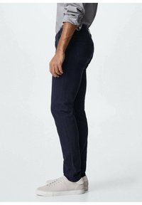 Tummansinisiä farkkuja, joissa on slim fit -malli, valmistettu denimistä. Sisältää takataskut ja vetoketjusuljennan. Yhdistetty vaaleanharmaisiin tennareihin.