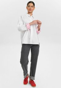 Camicia bianca con maniche a righe rosa, abbinata a jeans grigi con risvolto e sneakers rosse. Tessuto morbido e vestibilità rilassata.