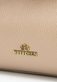 Sac à main en cuir beige avec une surface texturée, présentant un logo "Wittchen" en or et des détails complexes au-dessus du nom de la marque.