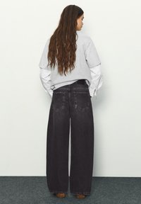 Džínsové nohavice s širokými nohavicami tmavosivej farby s dvoma zadnými vreckami, kombinované so sivým tričkom vrstveným cez biele tričko s dlhým rukávom.