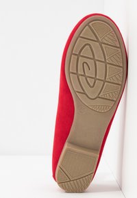 Semelle d'une chaussure plate rouge présentant une semelle extérieure en caoutchouc brun texturé avec motifs de bande de roulement pour l'adhérence, taille 37, sur fond blanc.