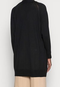 Cardigan negro de manga larga con un corte holgado, puños y dobladillo acanalados. Presenta una textura suave y un detalle de costura en la parte trasera.