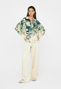 Floral patterned cream shirt with oversized sleeves, button-down front, paired with cream wide-leg pants and beige slip-on shoes.