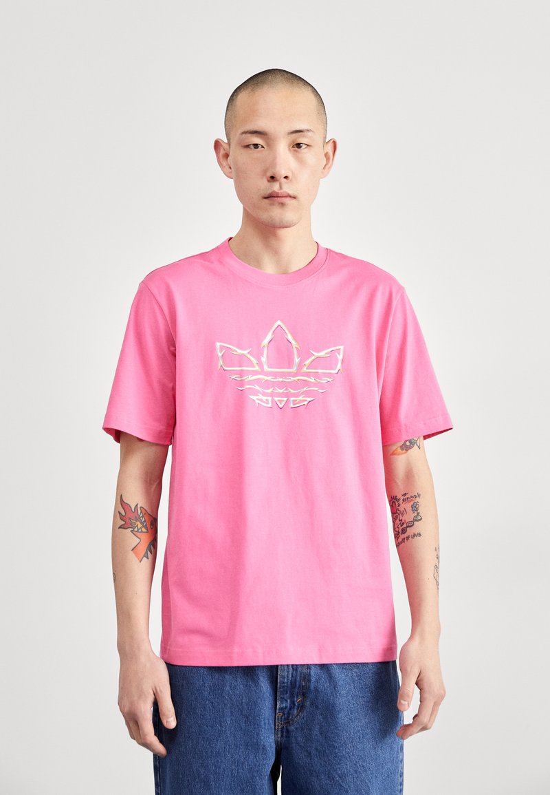 Pink cotton t-shirt with short sleeves, featuring a white graphic design in the shape of three stripes and a leaf emblem on the front.