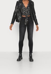 Giacca di pelle nera sopra un top corto floreale in bianco e nero, abbinato a jeans skinny neri con orlo sfilacciato e stivaletti neri.