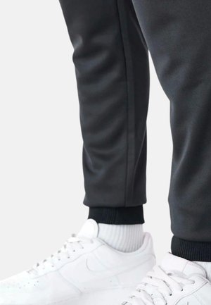Pantaloni sportivi grigio scuro con polsini a coste neri, abbinati a scarpe e calze sportive bianche. Il design è lineare con una delicata lucentezza.