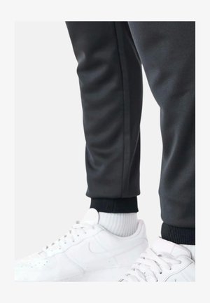 Pantaloni sportivi grigio scuro con polsini a coste neri, abbinati a scarpe e calze sportive bianche. Il design è lineare con una delicata lucentezza.