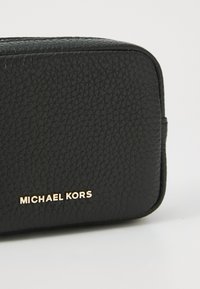 Black textured leather bag with rounded corners, featuring a gold "MICHAEL KORS" logo on the front. Compact design with a smooth zipper.