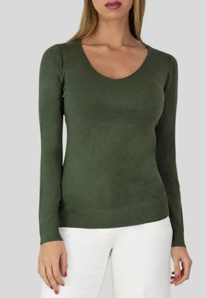 Pull long à manches longues vert olive avec un décolleté en scoop, texture lisse et design ajusté. Associé à un pantalon blanc.
