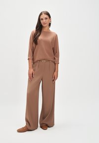 Brązowy sweter z dzianiny z rękawami 3/4, zestawiony z luźnymi, wysokim stanem brązowymi spodniami. Ubranie wzbogacone o pasek z prostokątną klamrą.