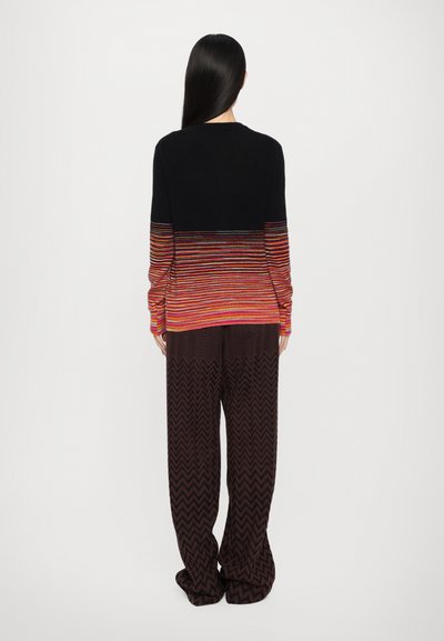 Knit sweater with black upper and multicolored striped lower. Paired with brown zigzag patterned wide-leg trousers. Soft texture.