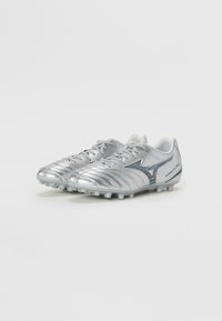 Ciorapi de fotbal argintii cu un finisaj texturat și accente albastre, având un design cu șireturi și piciorușe modelate pentru prindere pe gazon.