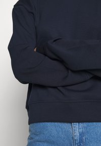 Felpa blu navy con collo a giro, maniche lunghe, polsini e orlo a costine. Il tessuto sembra morbido e liscio con una vestibilità comoda.