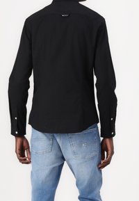 Czarna koszula na guziki z zaokrąglonym dołem, długimi rękawami i srebrnymi akcentami na guzikach, zestawiona z jasnoniebieskimi dżinsami.