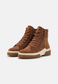 Bruna mocka högskor med snörning fram, sidogångjärn och en vit gummisula. Texturerad överdel med slitstarka sulor för bra grepp.