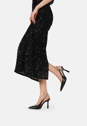 Zapatos de tacón negro tipo slingback con puntera afilada, que presentan un acento plateado brillante en la correa y un tacón de aguja. Textura de cuero suave.