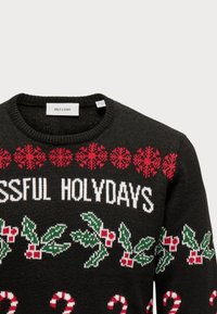 Schwarzer Strickpullover mit weißem Text "BLESSED HOLYDAYS", roten Schneeflocken, Zuckerstangen und einem Muster aus Stechpalmenblättern.