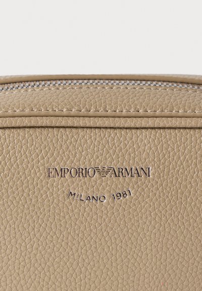 Τσάντα από ταμπά δέρμα με υφή στην επιφάνεια. Διαθέτει ασημένιο φερμουάρ και ανάγλυφο λογότυπο «Emporio Armani Milano 1981» στο μπροστινό μέρος.