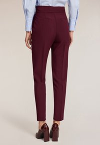 Bordeaux op maat gemaakte pantalons met een hoge taille, slim fit en een gladde textuur, met twee achterzakken en gedragen met glanzende hakken.