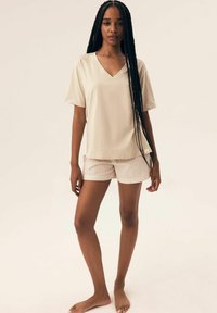 Beżowa koszulka z dekoltem w serek, luźny krój, w połączeniu z białymi spódniczkami w paski. Miękka faktura materiału, krótkie rękawy i casualowy design.
