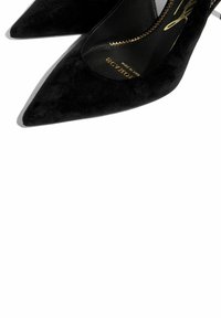 Crne suknje od nubuk kože s istaknutim špicastim vrhom. Imaju tanke potpetice i sjajan zlatni detalj sa zatvaračem duž unutarnje strane.