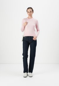 Maglione rosa chiaro a maniche lunghe, jeans dritti blu scuro e scarpe bianche slip-on. Design minimalista, texture liscia e silhouette semplice.