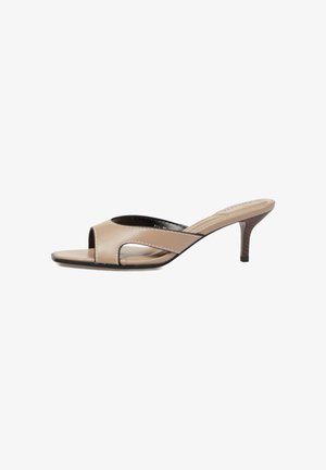 Zapato mule beige con puntera abierta, tacón bajo tipo kitten y detalle recortado en el lateral, sobre fondo blanco.