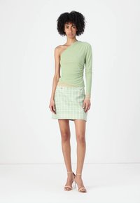 Lichtgroene top met één schouder en gerimpelde textuur, gecombineerd met een mintgroene geruite minirok. Het model draagt naakte, bandjeshakken.